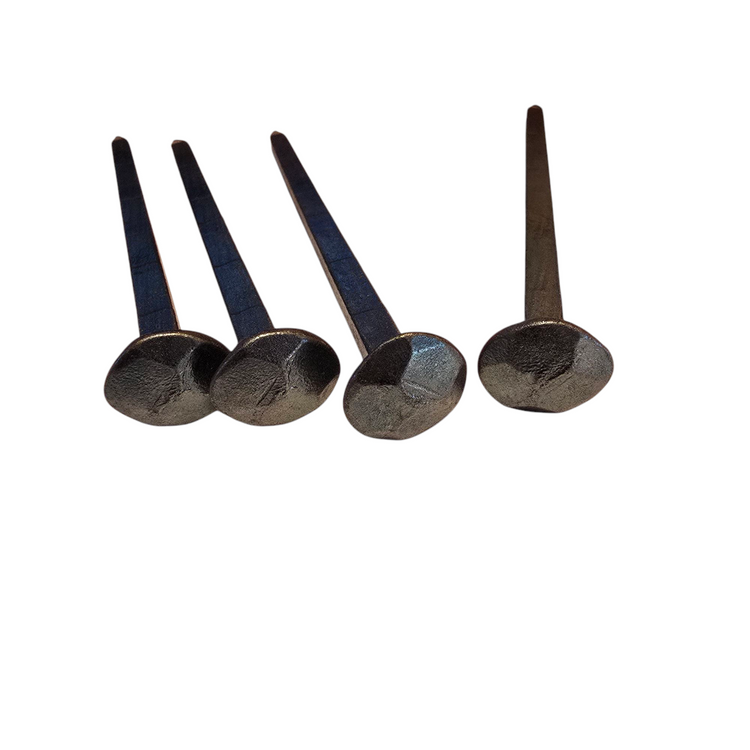 Vier handgeschmiedete Nägel mit gehämmertem Kopf auf weißem Hintergrund.