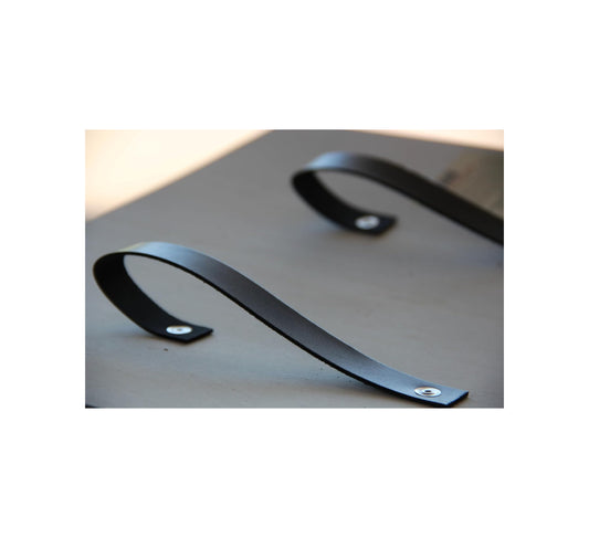 Zwei schwarze, gebogene Lederriemen mit Metallnieten sind auf einer hellen Holzfläche befestigt, als Griffe für ein Schild.