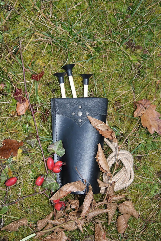 Schwarzer Pfeilköcher aus Leder mit Ziernieten, drei Sicherheits-Pfeile mit Saugnäpfen darin, daneben eine Kordel und Herbstlaub auf moosigem Boden.