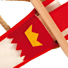 Detailansicht eines Holzspielzeug-Schwerts mit rotem Griffband, gesteckt in eine weiße Scheide mit rotem Besatz und gelbem Kronenmotiv.