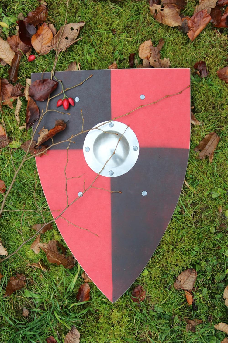  Tropfenförmiger Schild mit rot-schwarzem Viertelmuster und zentralem Metallschildbuckel, liegend auf grünem Moosboden mit Herbstlaub, Hagebutten und Zweigen.