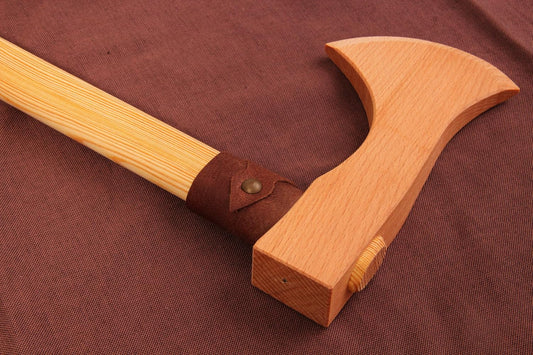 Nahaufnahme einer Holz-Wurfaxt mit hellem Griff, brauner Ledermanschette und geschwungener Klinge aus Buchenholz. Die Axt liegt auf braunem Stoff.